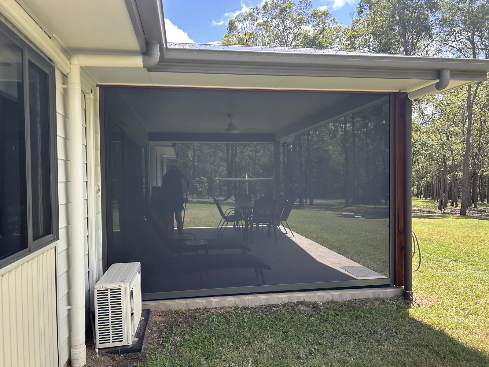 ZipScreen mesh blind fully enclosing a Queensland patio, with outdoor dining setting visible through the see-through fabric