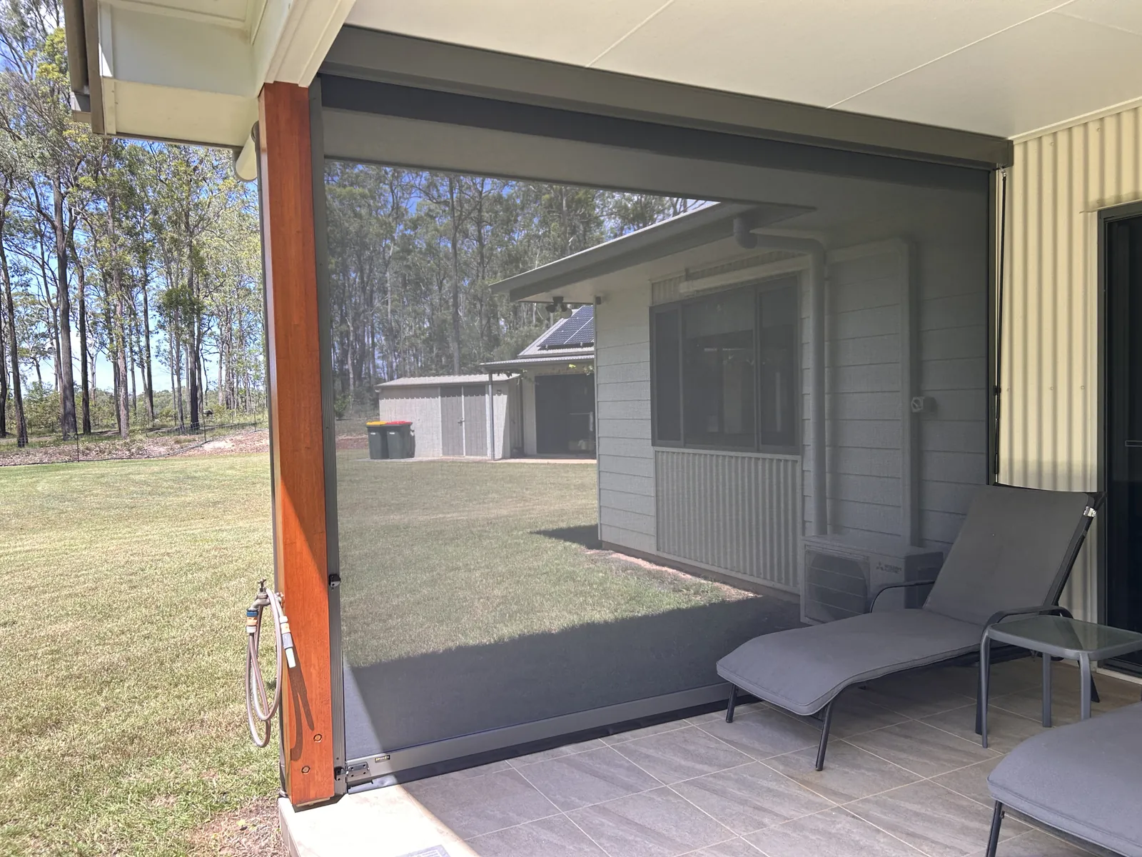 ZipScreen outdoor blind on a timber-post alfresco with sun lounge, keeping the view of the lawn through the mesh