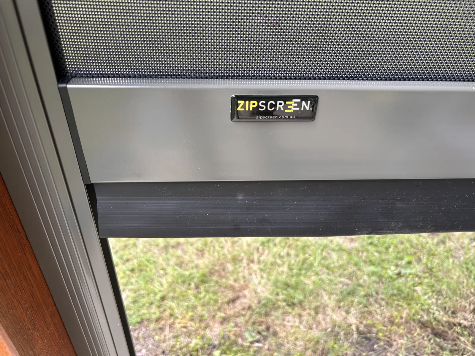 Close-up of a Zipscreen-branded aluminium headbox and weighted bottom bar with UV-stable mesh fabric